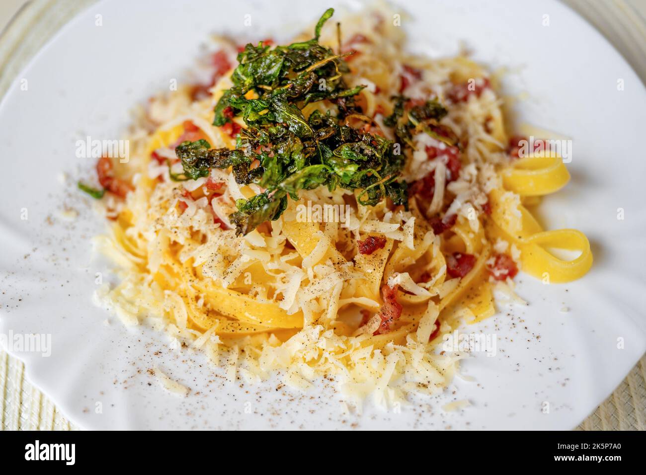 Tagliatelle italienne bouillie avec bacon en cubes frits, fromage râpé et roquette frite sur plaque blanche, restaurant en plein air. Banque D'Images