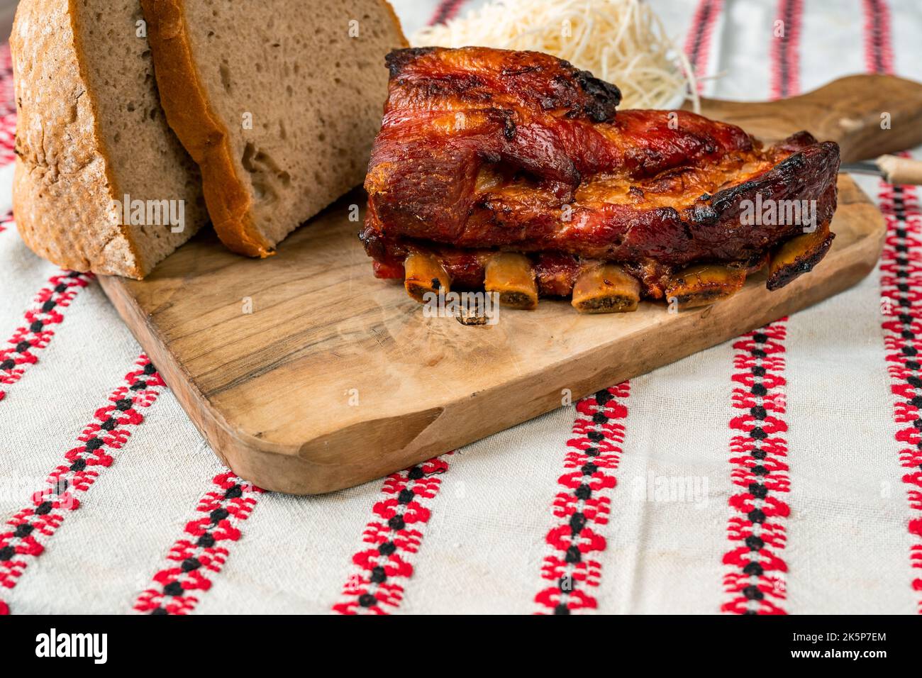 Côte de porc cuite avec pain coupé en tranches et raifort râpé sur un plan de cuisine en bois, nappe rustique, gros plan. Banque D'Images