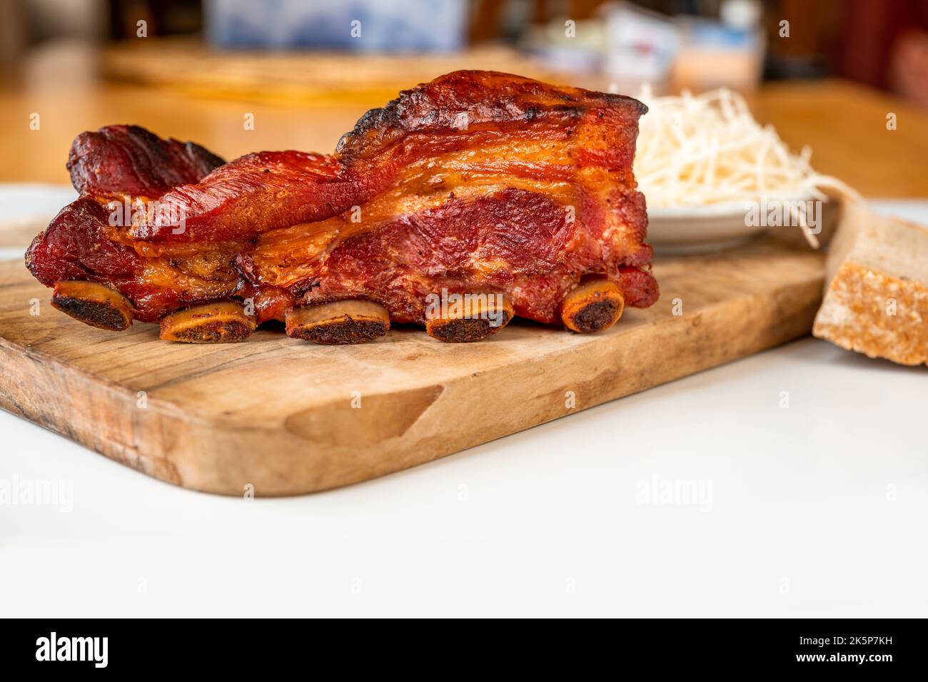 Morceau de côte de porc juteuse cuite avec croûte croustillante sur le plan de cuisine en bois avec raifort râpé sur la table, en gros plan. Banque D'Images