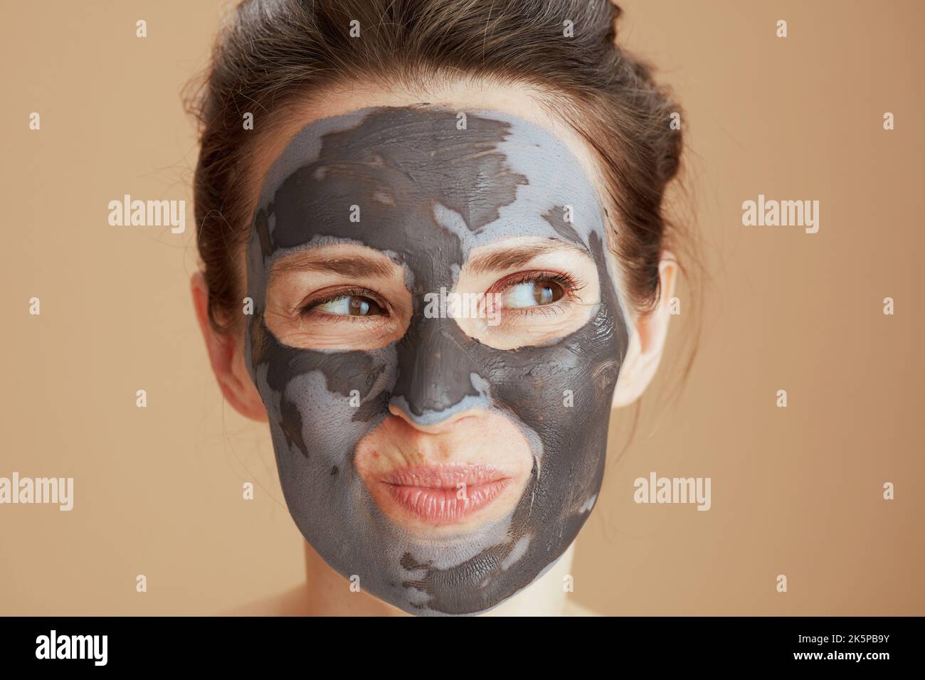 femme pensive de 40 ans avec masque cosmétique isolée sur fond beige. Banque D'Images