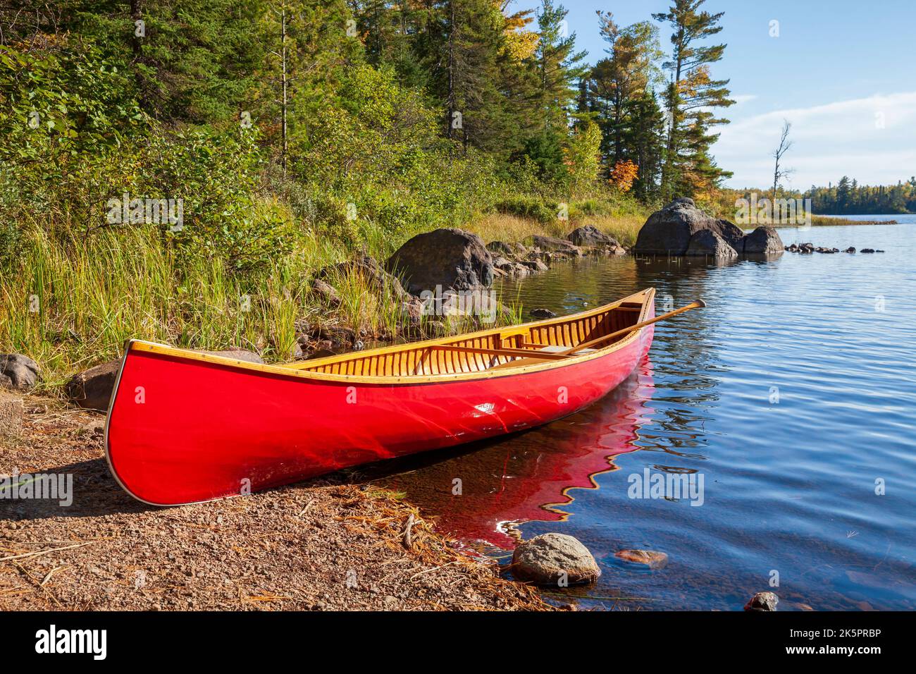 Canoë en bois rouge sur la rive du lac du nord du Minnesota avec des rochers et des pins le long de la rive Banque D'Images