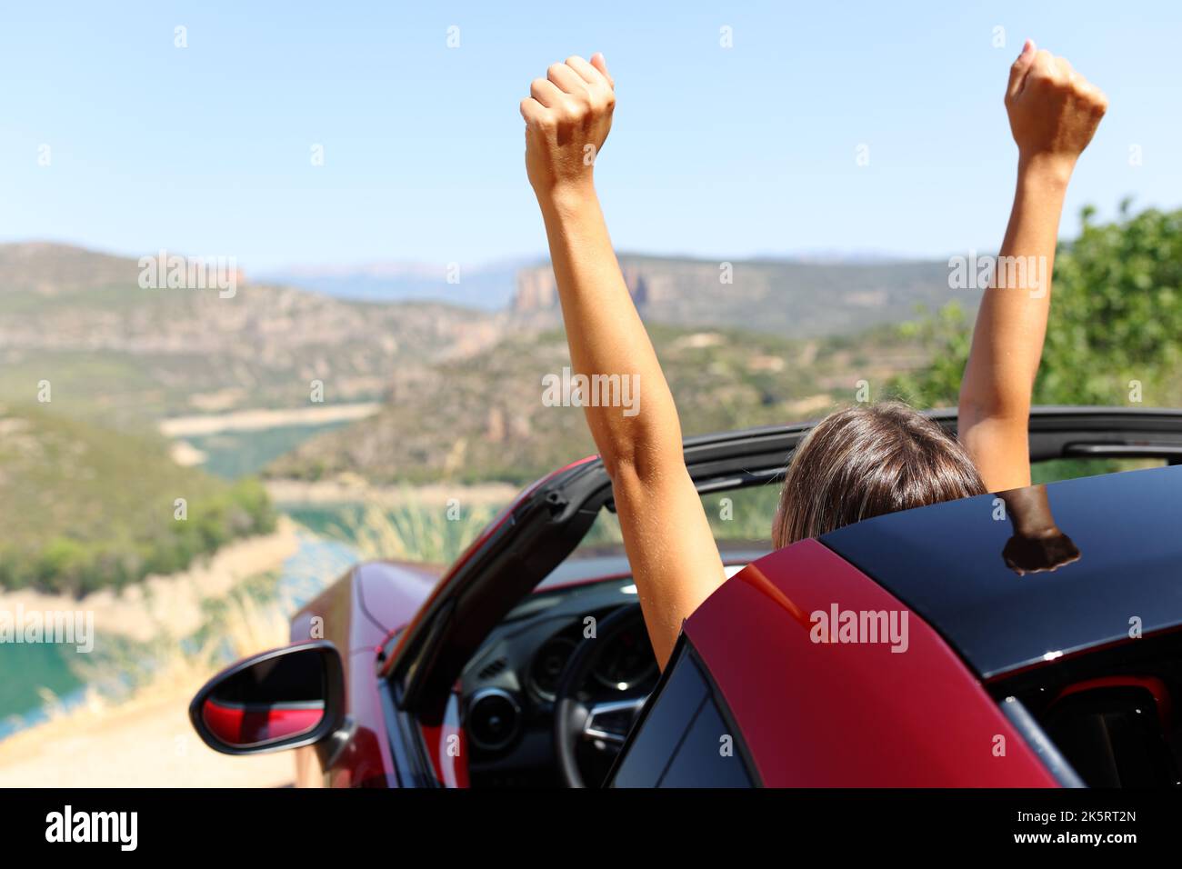 Portrait arrière d'une femme heureuse dans une voiture décapotable levant les bras Banque D'Images