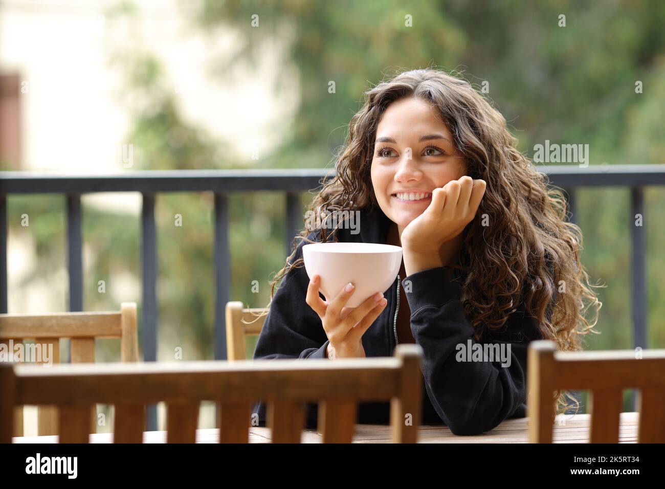 Bonne femme tenant un bol contemplant le petit déjeuner sur un balcon Banque D'Images
