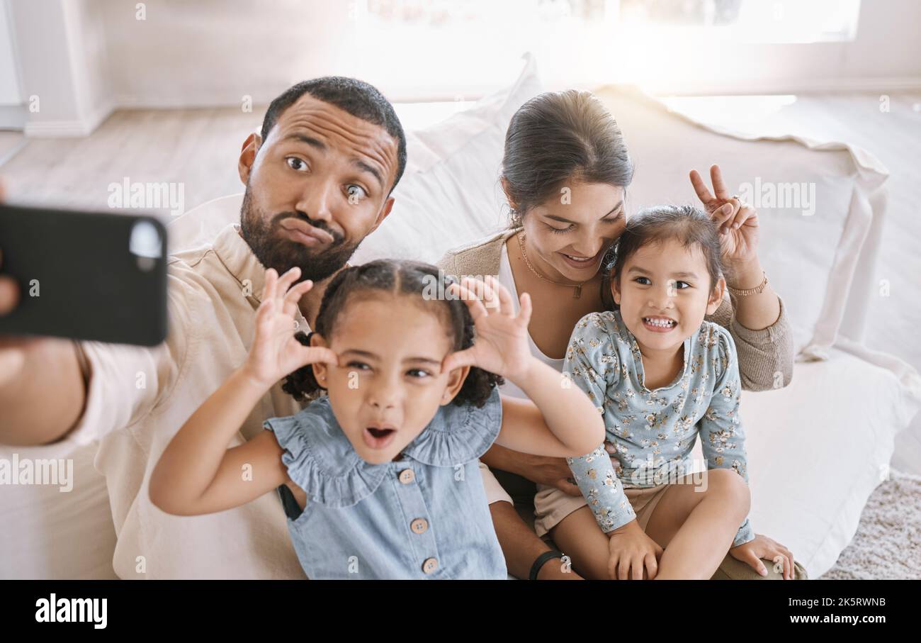 Portrait d'une famille de race mixte prenant un selfie et faisant des visages drôles tout en étant assis sur le canapé à la maison. Homme hispanique utilisant un smartphone pour prendre un Banque D'Images