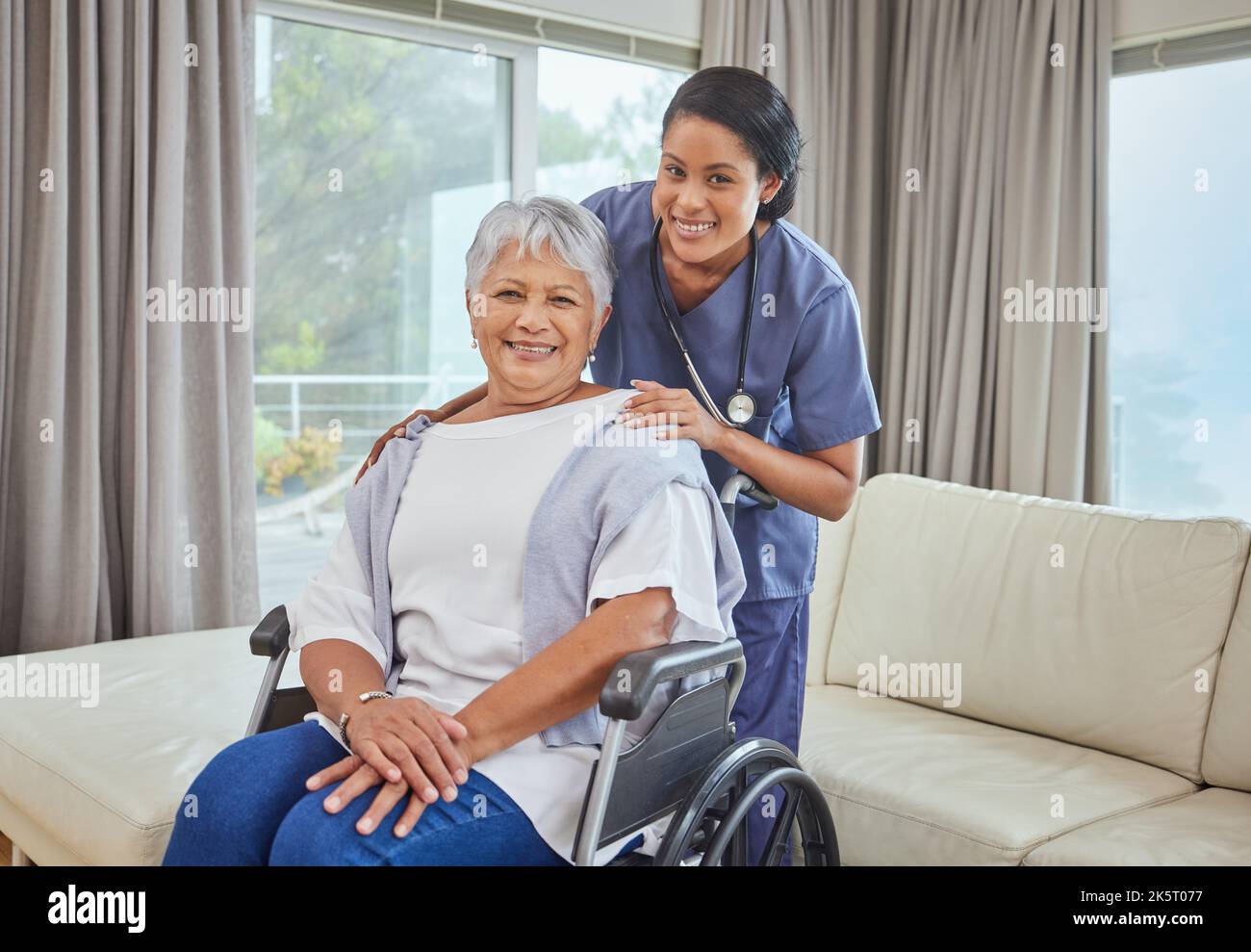 Portrait d'une femme hispanique âgée en fauteuil roulant et de son infirmière féminine dans la maison de la vieillesse. Jeune infirmière de race mixte et sa patiente dans le salon Banque D'Images