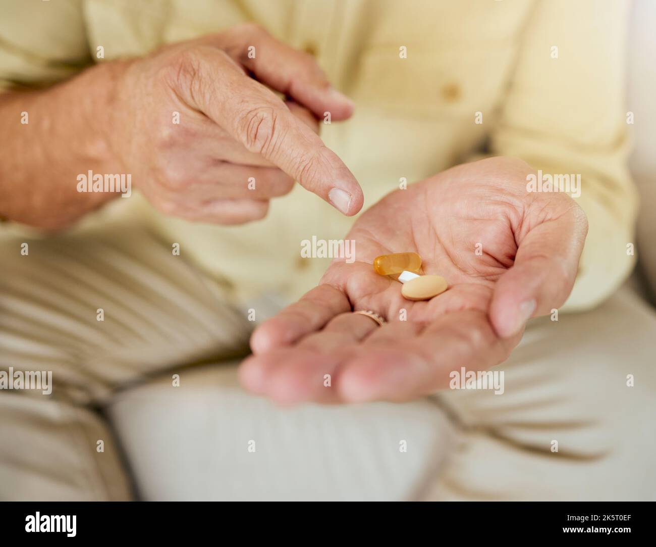 Un inconnu montrant ses pilules en étant assis à la maison. Homme mature méconnaissable prenant son traitement quotidien pour les maladies chroniques Banque D'Images