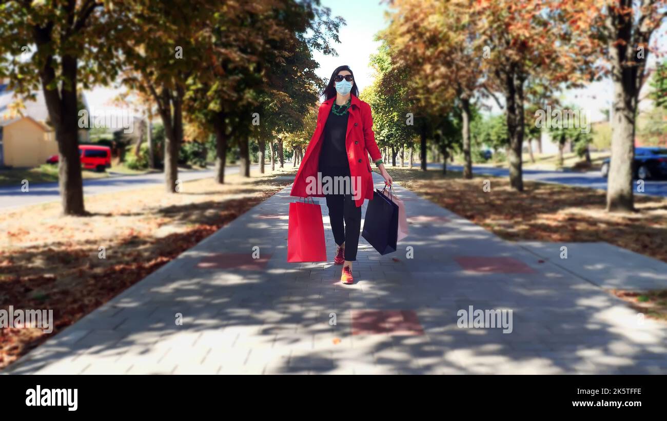 Femme avec des sacs de shopping. Femme, dans un masque de protection, avec des sacs de shopping colorés dans ses mains, marchant dans une allée de ville. Shopping et cadeaux. Livraison ou concept de don. Photo de haute qualité Banque D'Images