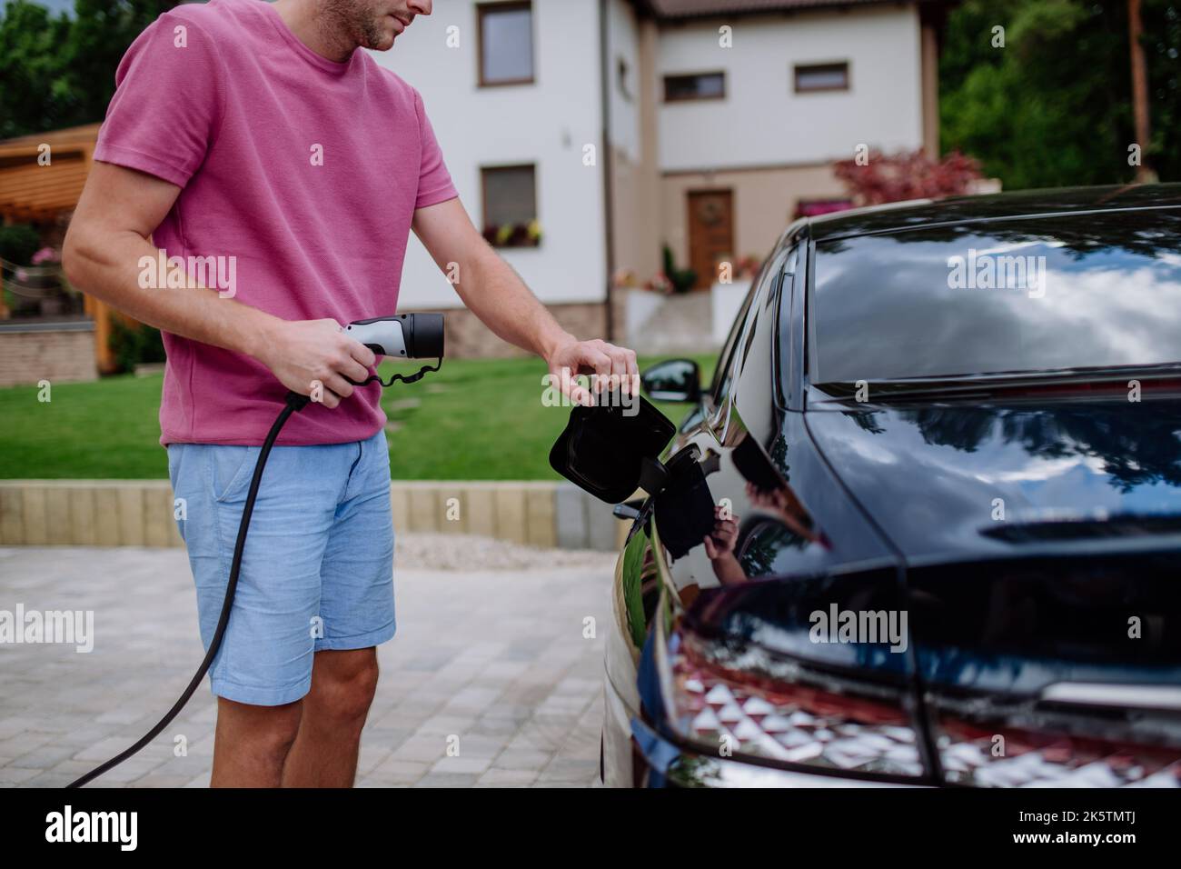 Homme tenant le câble d'alimentation électrique à la station de charge du véhicule électrique. Banque D'Images