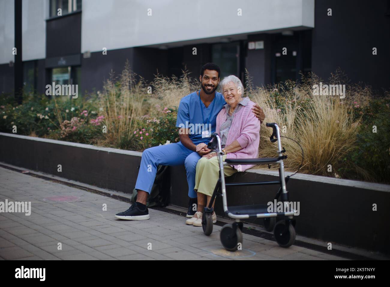 Heureuse femme âgée assise et parlant avec un assistant médical devant la maison nourissante. Banque D'Images