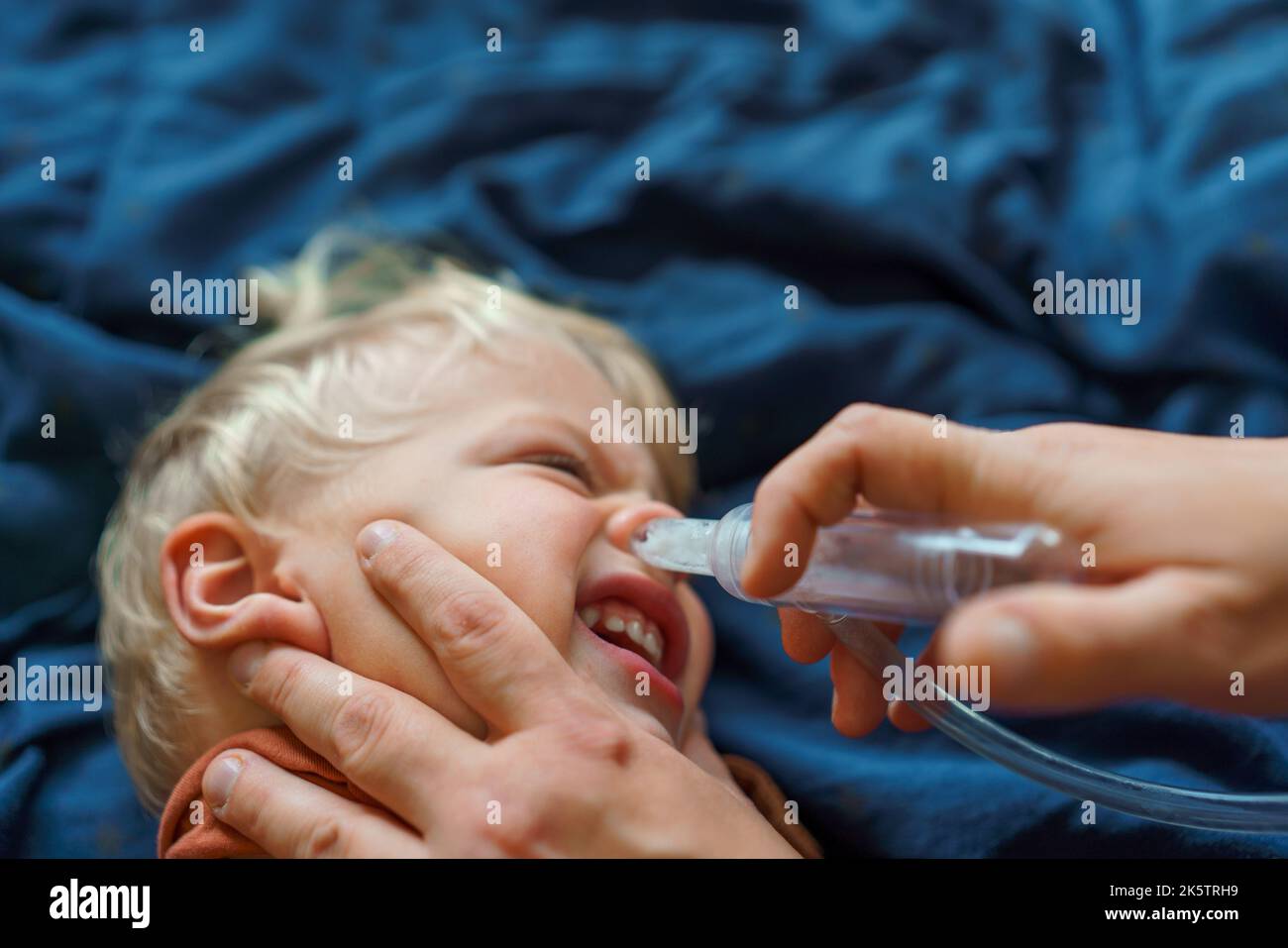 Gros plan du parent tenant son fils et utilisant un extracteur de snot. Banque D'Images