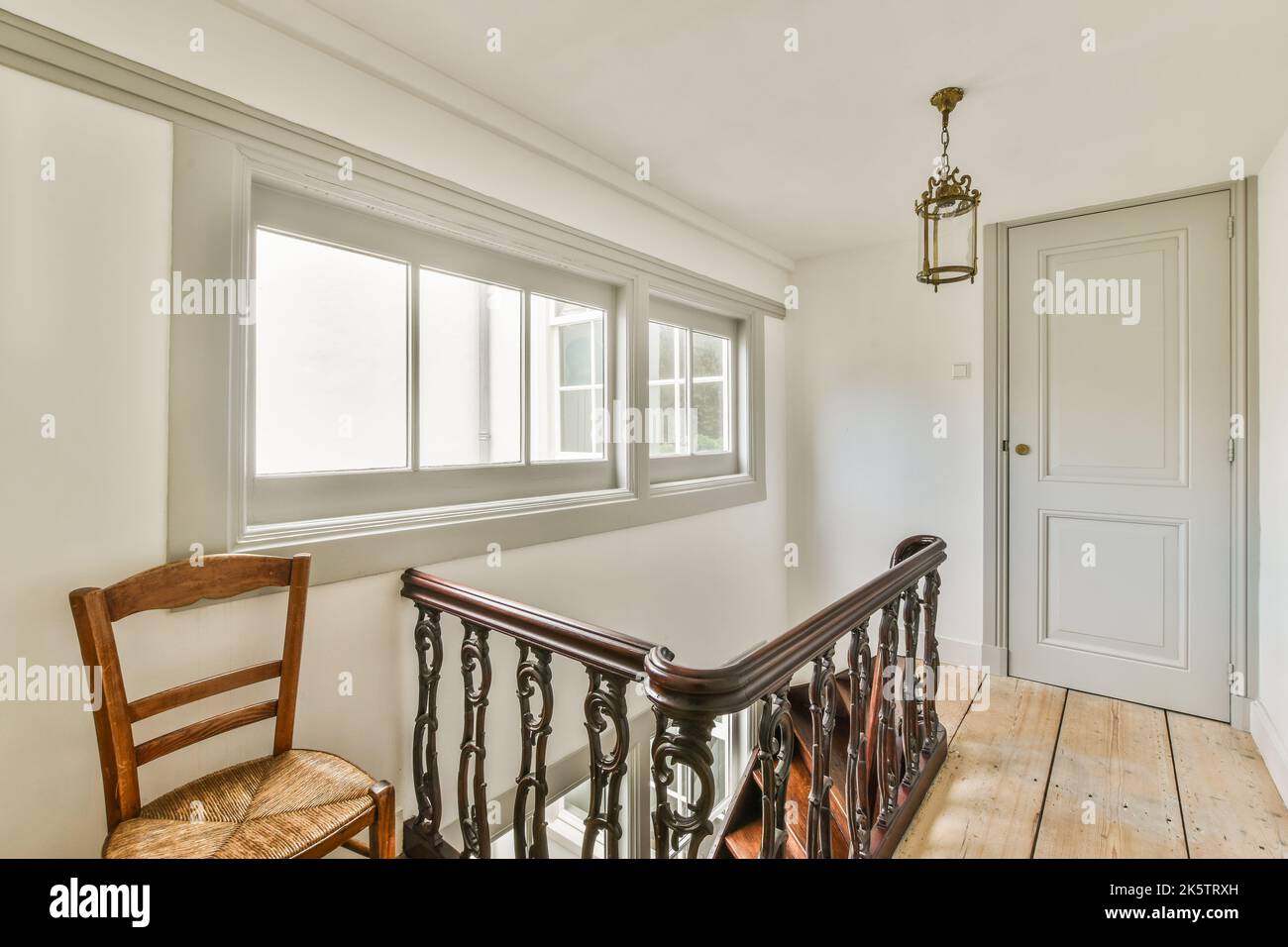 Couloir étroit et lumineux avec porte aux murs blancs et lampe au-dessus du sol en bois Banque D'Images