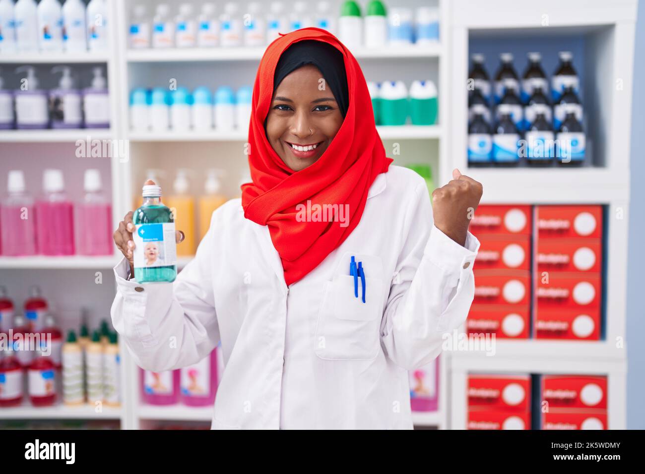 Jeune femme arabe travaillant à pharmacie drugstore tenant le sirop criant fier, célébrant la victoire et le succès très excité avec le bras levé Banque D'Images