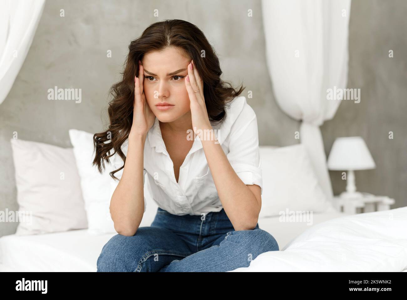 Bouleversée jeune femme déprimée, assise au lit, sensation de maux de tête sévères, migraine, triste femme fatiguée, épuisée après tension nerveuse et stress. Banque D'Images