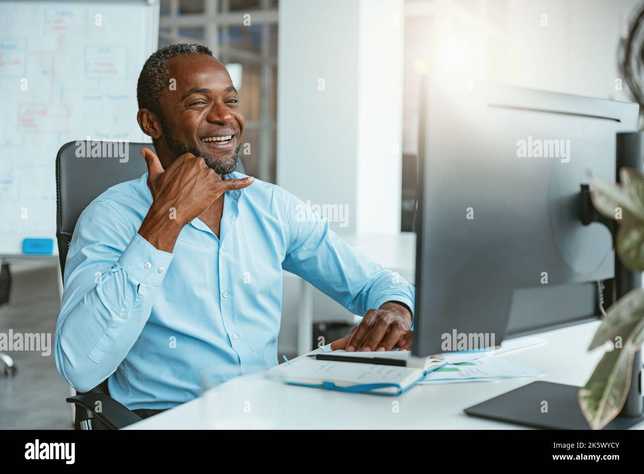 Homme d'affaires africain utilisant le langage des signes tout en parlant en ligne avec le client assis au bureau Banque D'Images