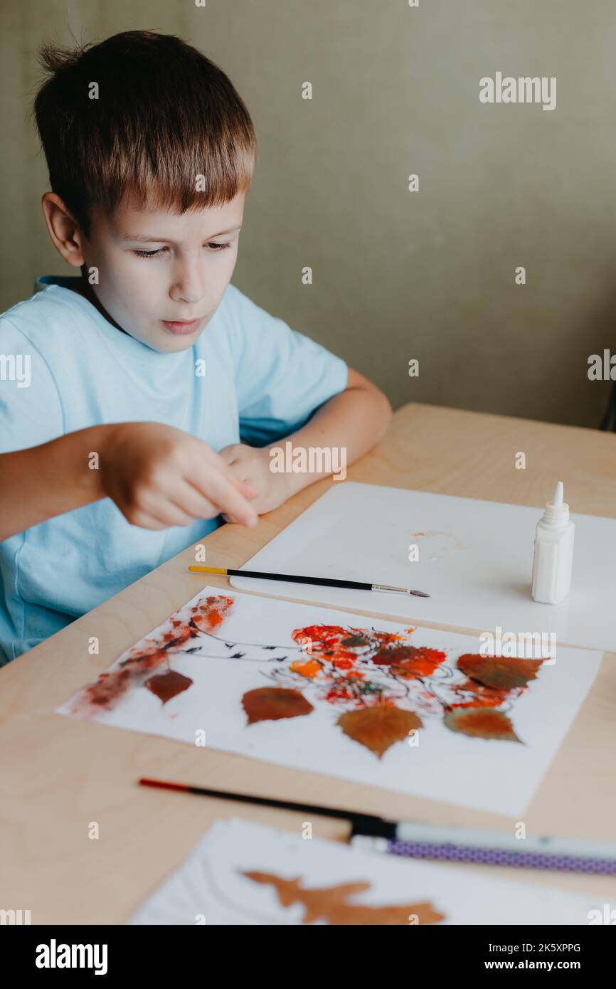 Enfant mignon assis au bureau et faisant la photo de feuilles de bouleau sec Banque D'Images