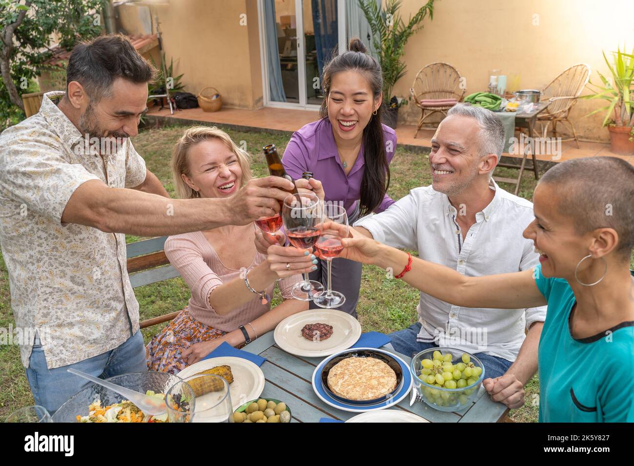 Des amis qui toastent avec un beau sourire autour de la table dans le patio de la maison. Banque D'Images
