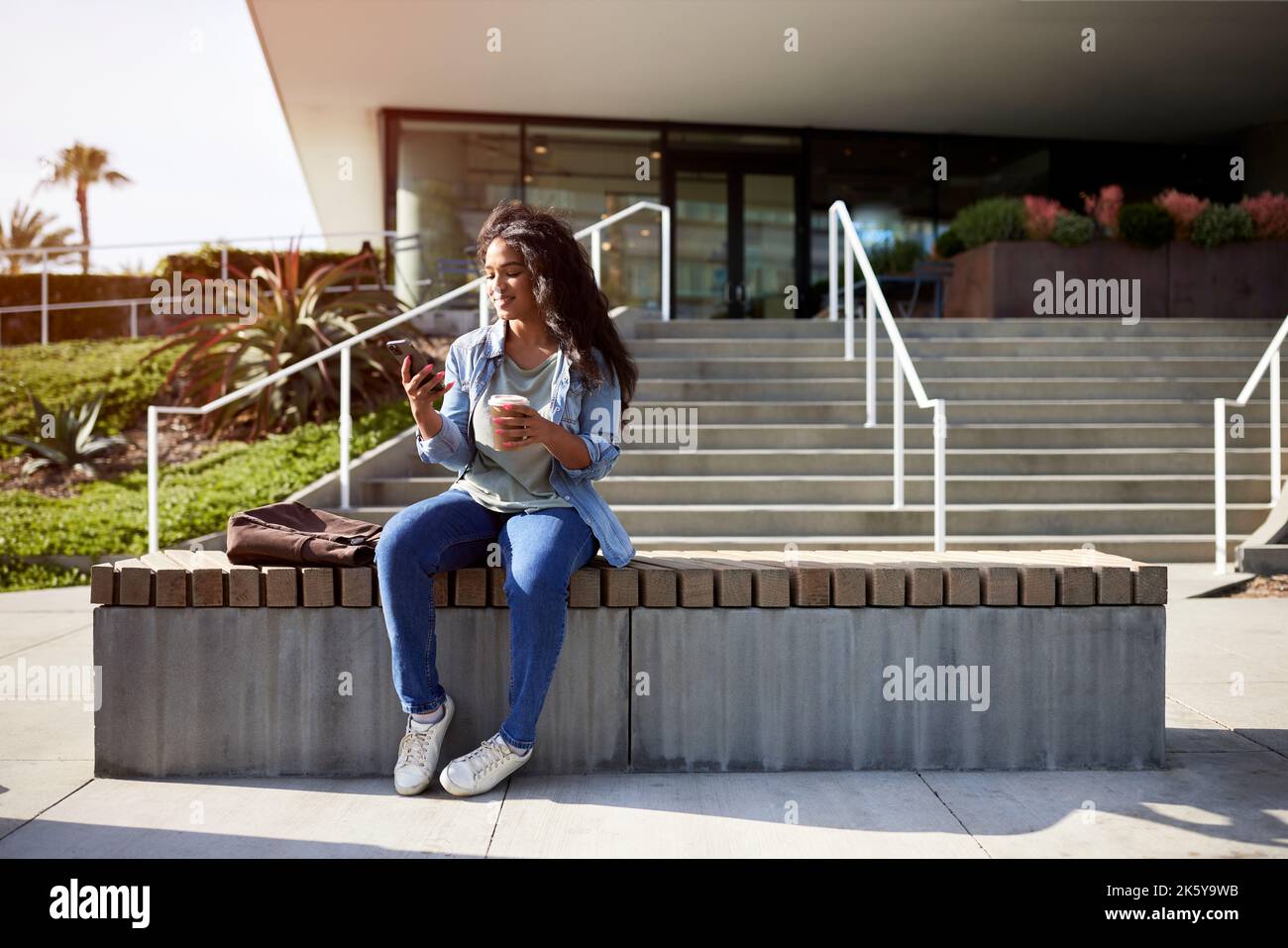 Femme souriante utilisant un smartphone assis sur un banc Banque D'Images