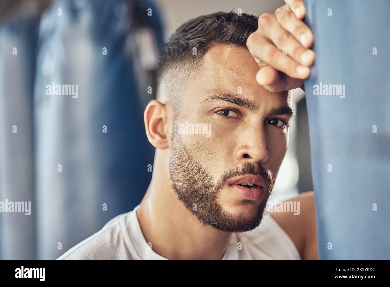 Boxeur fatigué prenant une pause de la routine cardio. Portrait d'un combattant mma épuisé appuyé sur un sac de poinçonnage. Bodybuilder prend une pause de combat Banque D'Images