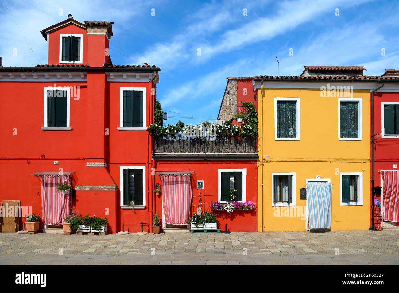 Maisons rouges et jaunes lumineuses situées contre le ciel bleu nuageux le jour ensoleillé sur la rue de l'île de Burano en Italie Banque D'Images