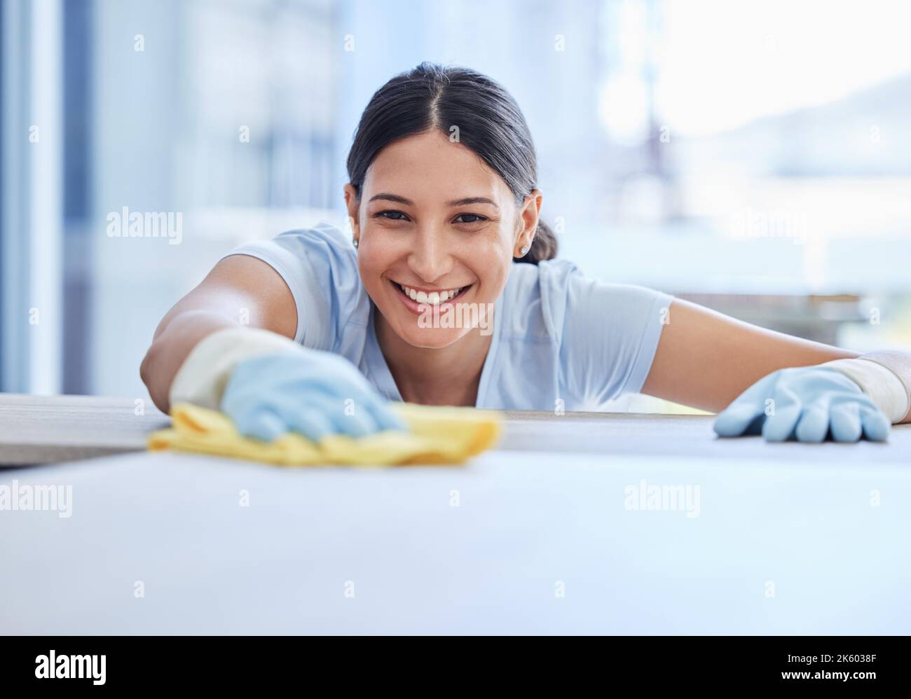 Une belle jeune femme de race mixte souriante qui nettoie les surfaces de sa maison. Un travailleur domestique hispanique heureux essuyant une table Banque D'Images