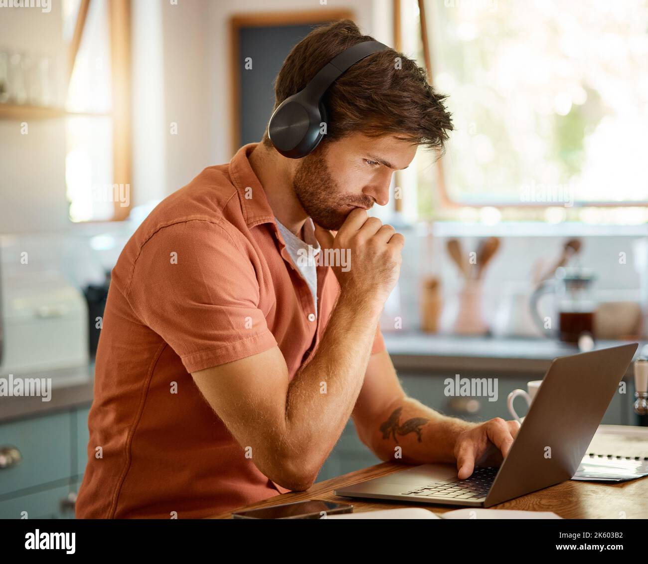 Jeune homme d'affaires caucasien sérieux portant des écouteurs et écoutant de la musique tout en utilisant un ordinateur portable à la maison seule. Un homme d'affaires spécialisé Banque D'Images