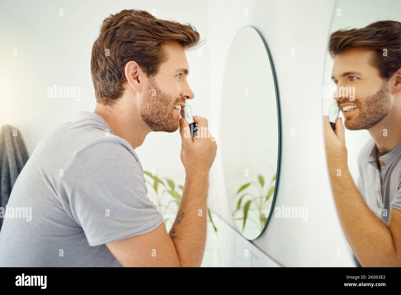 Un beau homme taille ses cheveux de nez dans une salle de bains à la maison. Homme caucasien utilisant un coupe-nez tout en regardant dans un miroir dans son appartement Banque D'Images