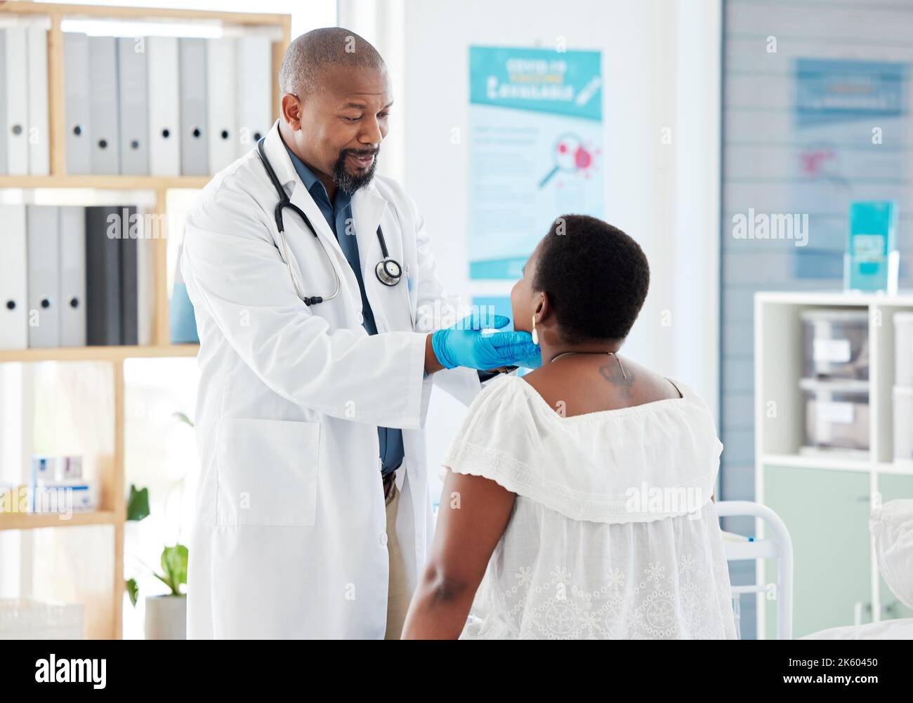 Un médecin afro-américain mature vérifie la gorge d'un patient. Patient en examen avec son médecin. médecin généraliste vérifiant le mal de gorge du patient Banque D'Images