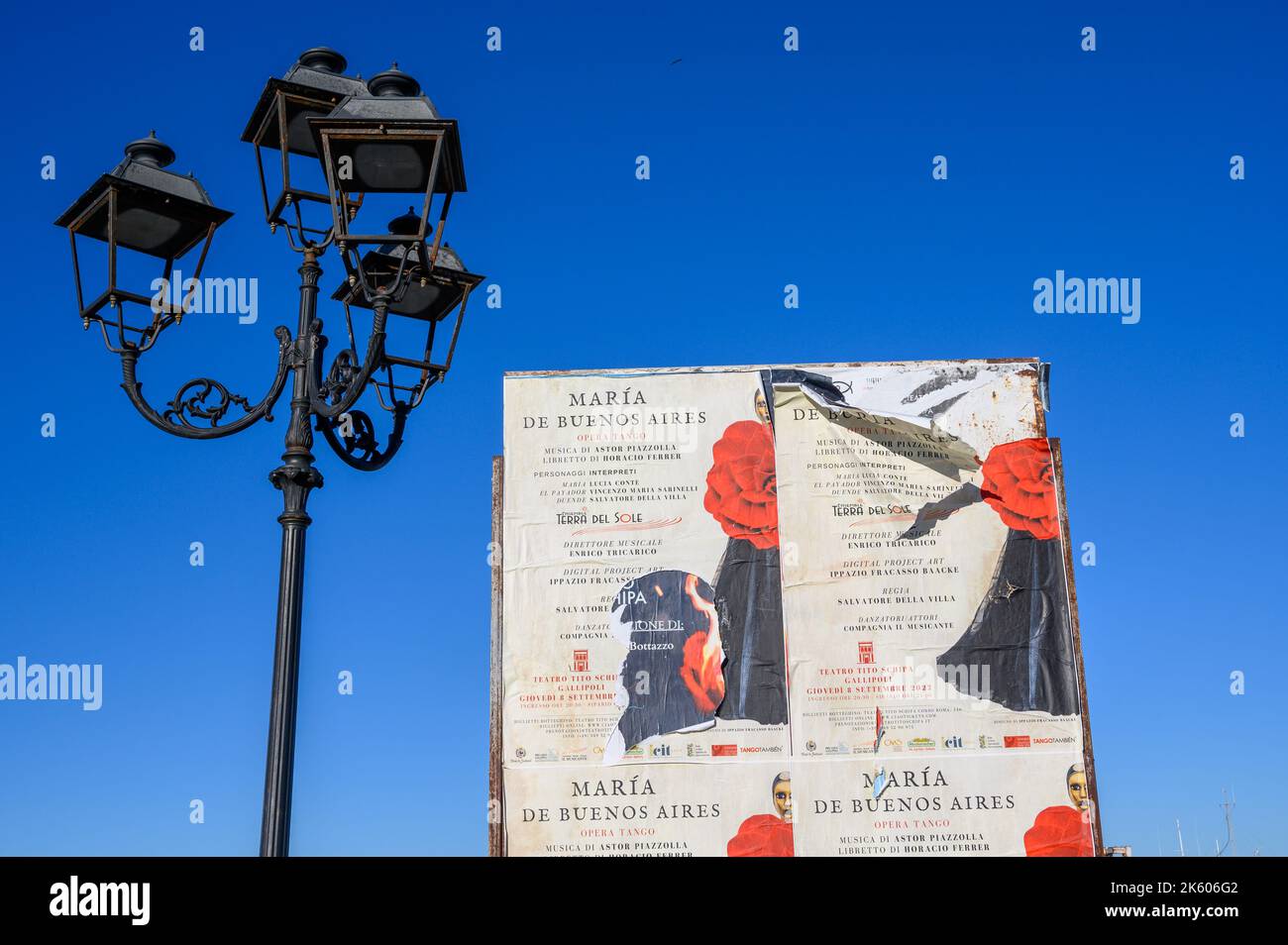 Ancien lampadaire en fer forgé et des affiches contre le ciel bleu profond faisant la promotion d'une performance d'opéra à Gallipoli, en Italie Banque D'Images