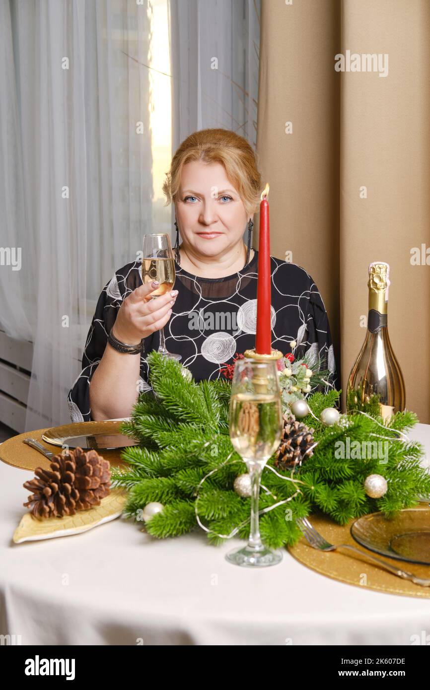 Joyeuse femme d'âge moyen célébrant noël assis derrière la table de fête Banque D'Images