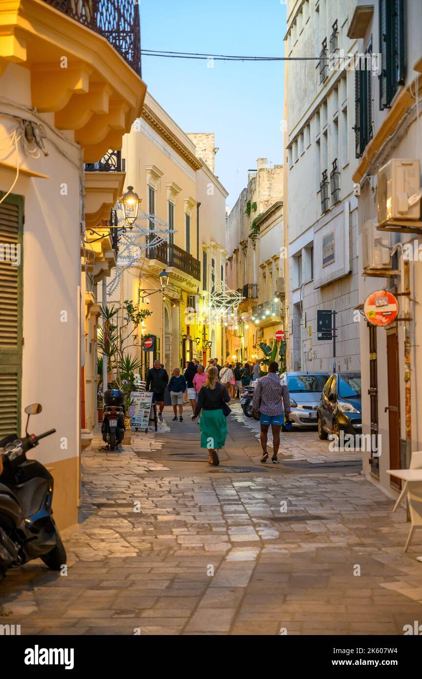 Touristes et habitants marchant le long d'une rue typique étroite et pavée dans la vieille ville de Gallipoli en début de soirée, Apulia (Puglia), Italie. Banque D'Images