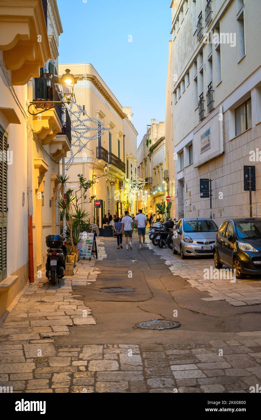 Touristes et habitants marchant le long d'une rue typique étroite et pavée dans la vieille ville de Gallipoli en début de soirée, Apulia (Puglia), Italie. Banque D'Images