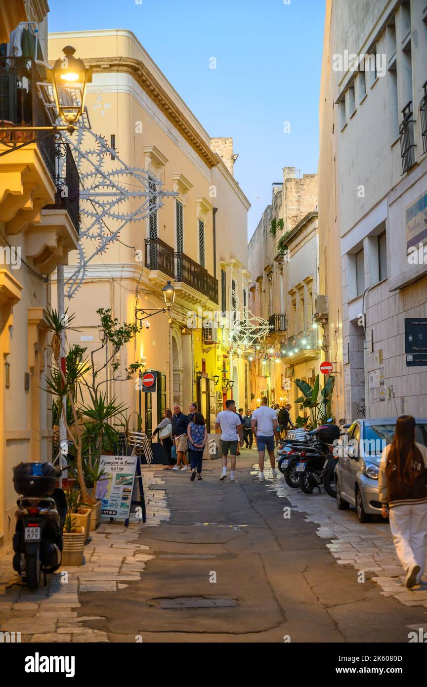 Touristes et habitants marchant le long d'une rue typique étroite et pavée dans la vieille ville de Gallipoli en début de soirée, Apulia (Puglia), Italie. Banque D'Images