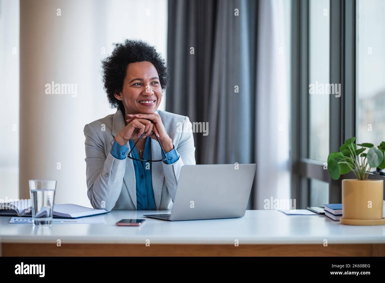 Joyeuse femme de direction d'entreprise afro-américaine dans un costume, prenant un reniflard, au bureau. Banque D'Images