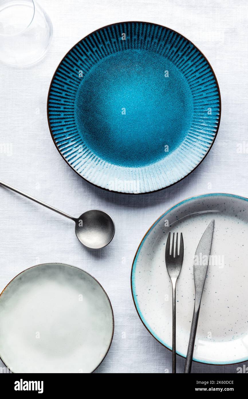 Ensemble de vaisselle moderne avec une assiette bleu vif, des couverts et un verre, plan de dessus plat. Vaisselle tendance sur une nappe Banque D'Images