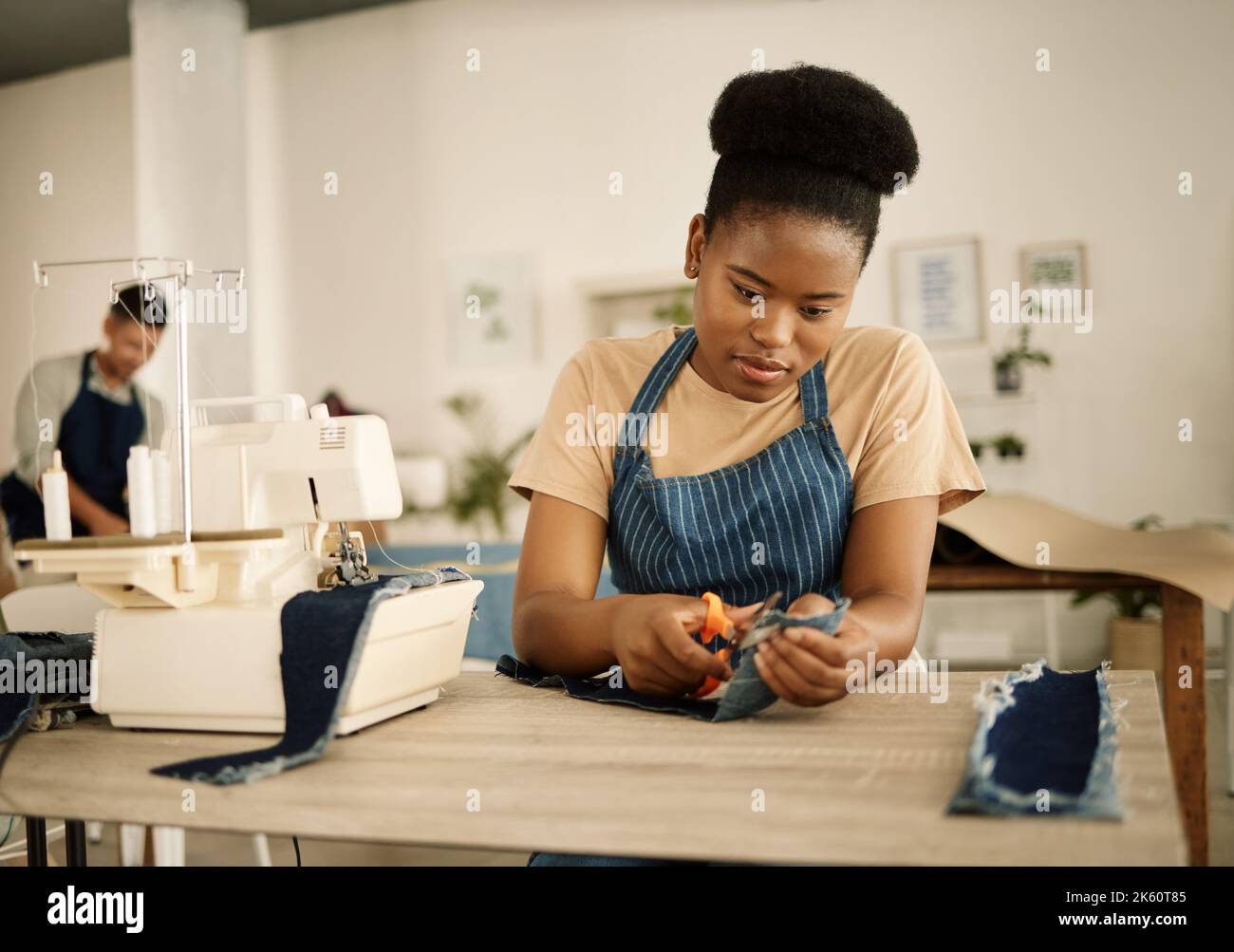 Un designer de mode afro-américain taillé un morceau de denim. Travailler sur mesure dans son studio. Couturière découpage d'un morceau de tissu à l'aide d'un ciseau Banque D'Images