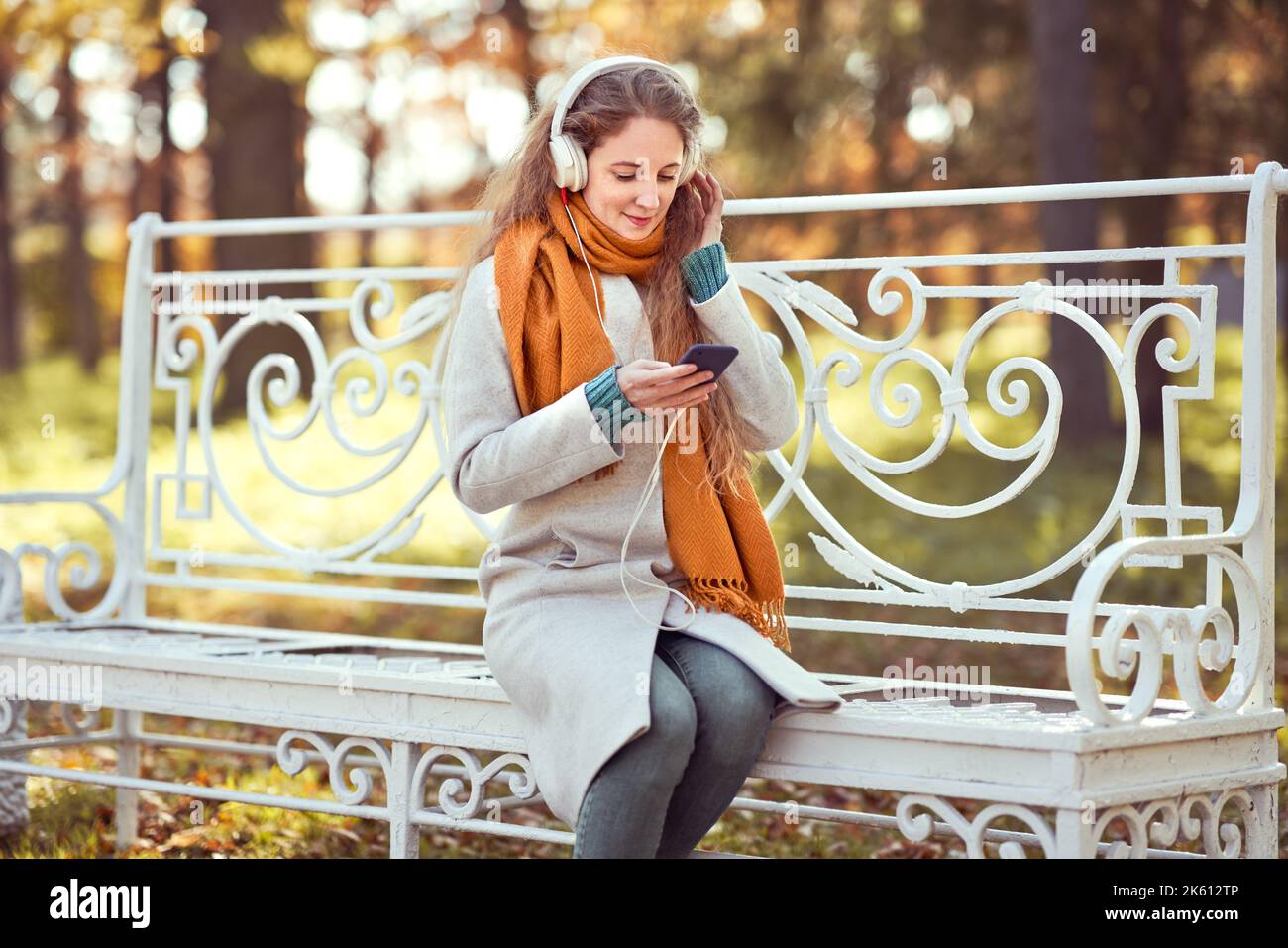 Une jeune femme aux cheveux rouges est assise sur un banc dans un parc d'automne. Une fille écoute de la musique dans la forêt d'automne Banque D'Images