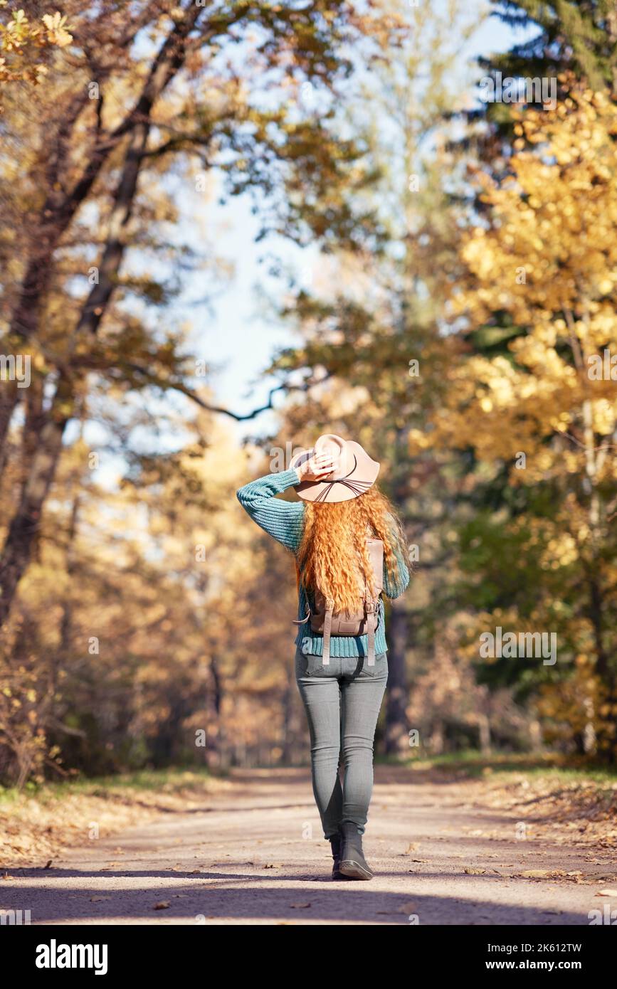 Une jeune femme aux cheveux rouges se promène dans le parc d'automne. Une fille dans un chapeau beige regarde la forêt d'automne Banque D'Images