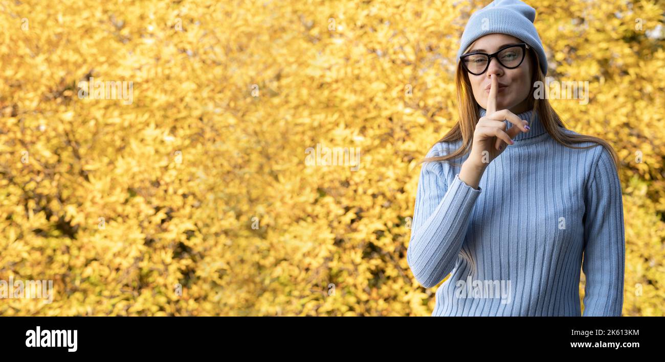 Jeune fille avec geste de silence sur fond de feuillage d'automne jaune. Concept d'automne. Bannière, place pour la publicité Banque D'Images