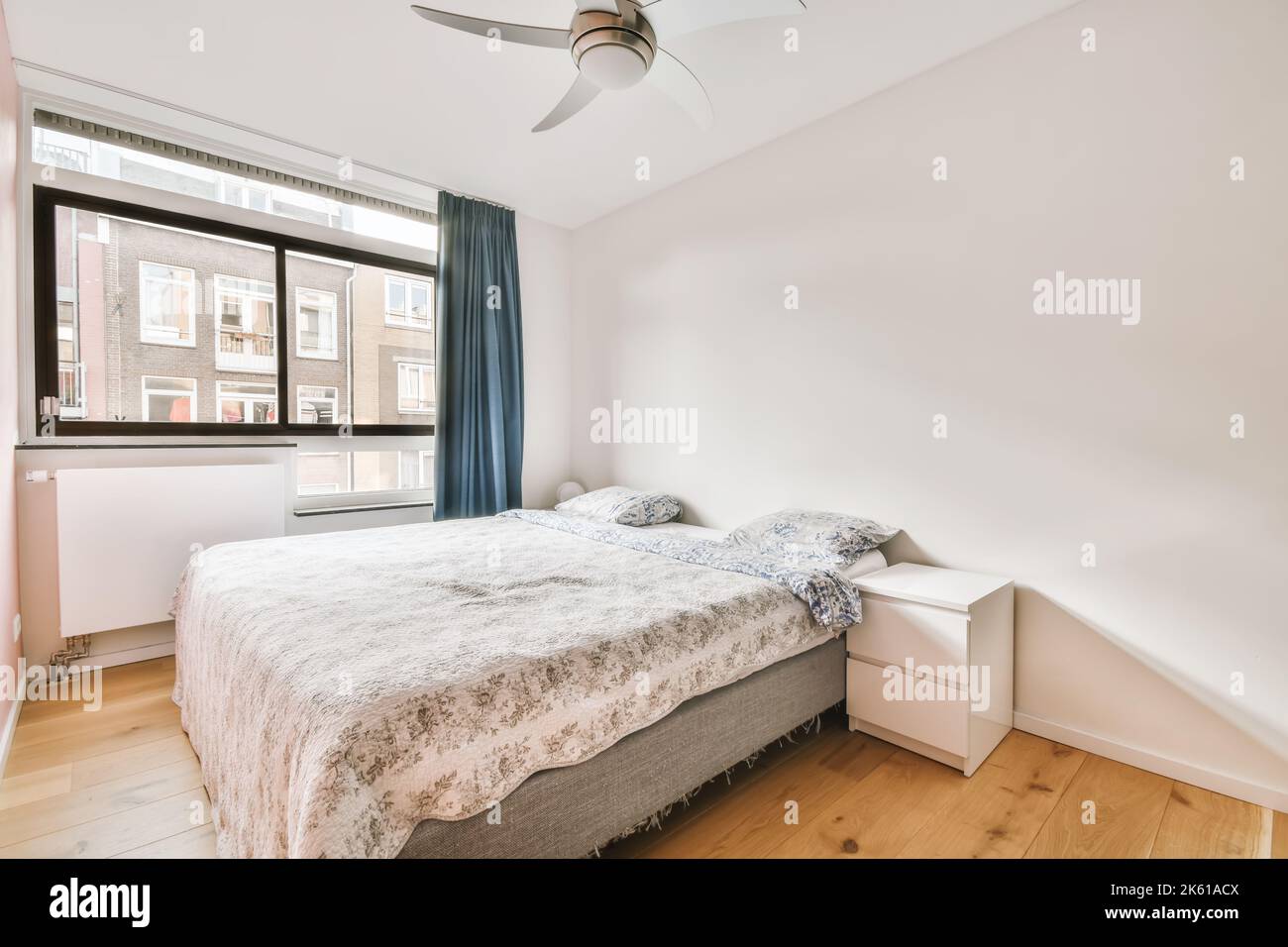 Lit confortable avec couverture et oreillers placés près de la fenêtre dans une chambre lumineuse avec table de nuit et commode dans une maison moderne Banque D'Images