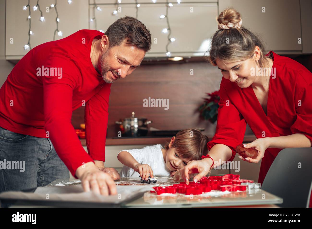 Atmosphère de bonheur, confort de Noël. La famille, le père, la mère et le fils cuisent des biscuits dans une cuisine confortable à la maison. Vêtu de rouge. Travail d'équipe. Banque D'Images