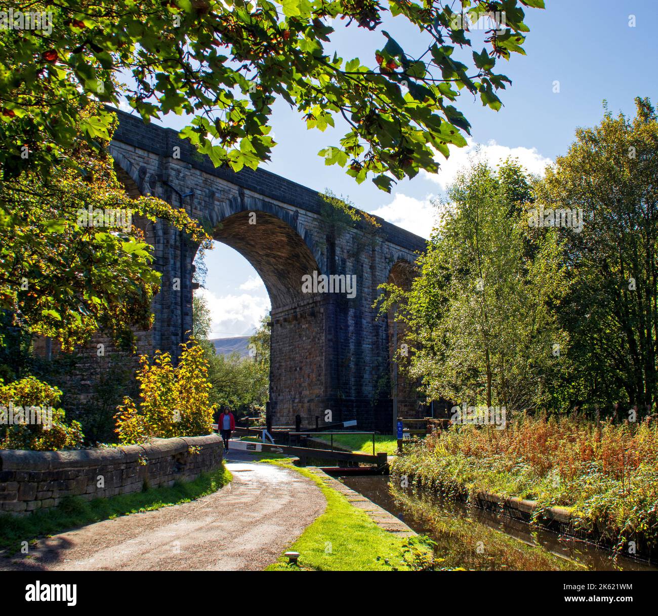 En regardant le chemin sous un viaduc ferroviaire historique, le long d'une écluse sur le canal étroit de Huddersfield, à Uppermill, Oldham, Banque D'Images