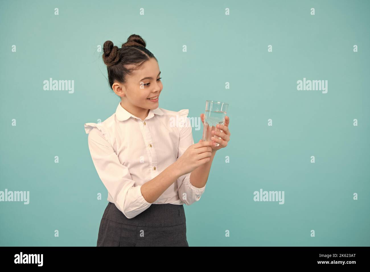 Une jeune fille adorable boit de l'eau en verre sur fond bleu. Bonne adolescente, émotions positives et souriantes de la jeune fille. Banque D'Images