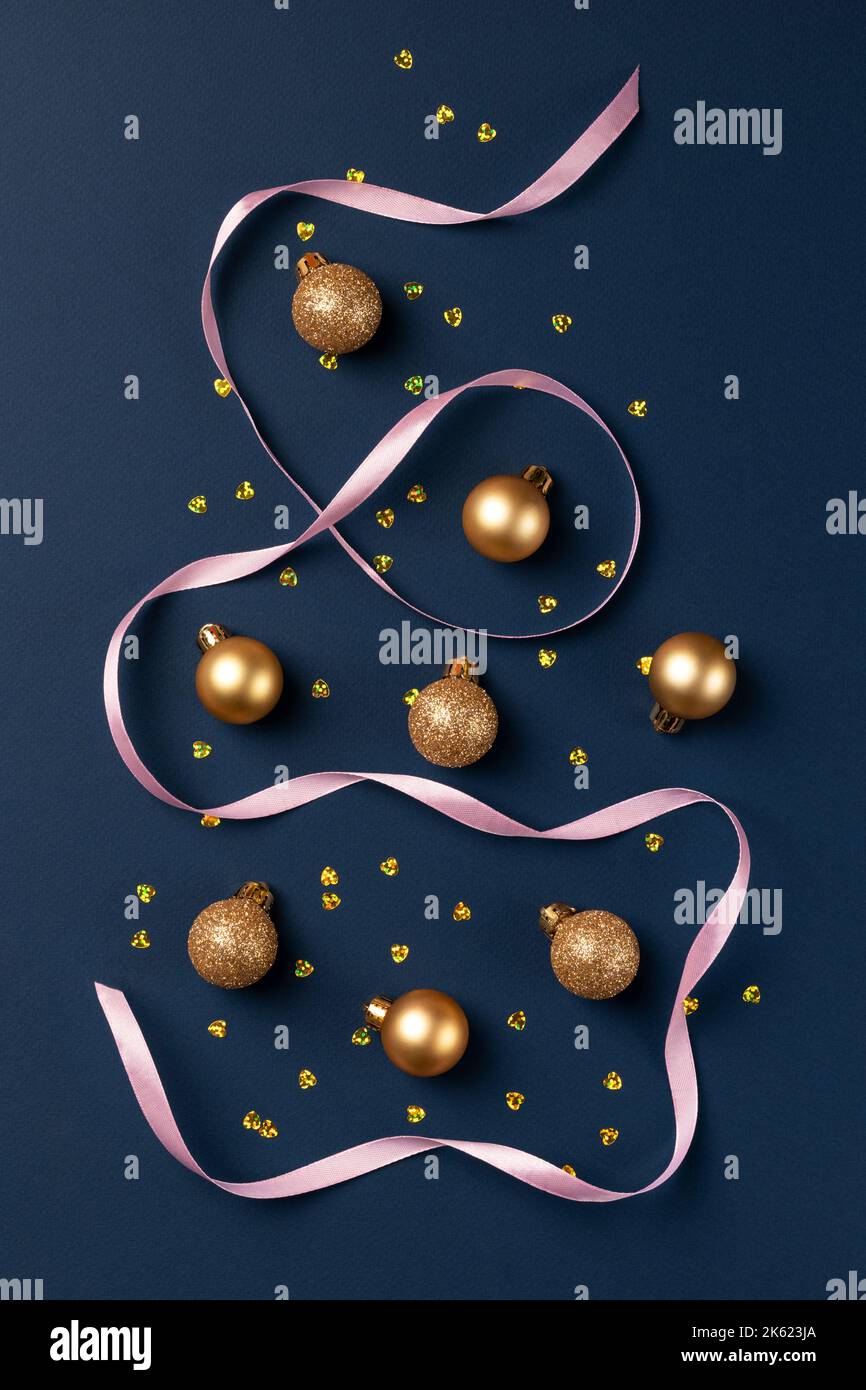 Carte de Noël avec boules dorées à paillettes, confetti et ruban en satin sur fond bleu foncé Banque D'Images