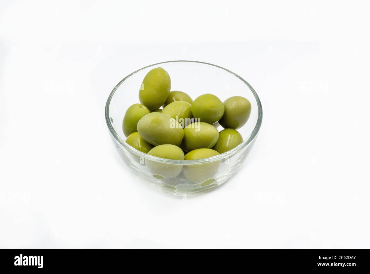 Les olives vertes entières se ferment dans un bol en verre transparent sur du blanc Banque D'Images