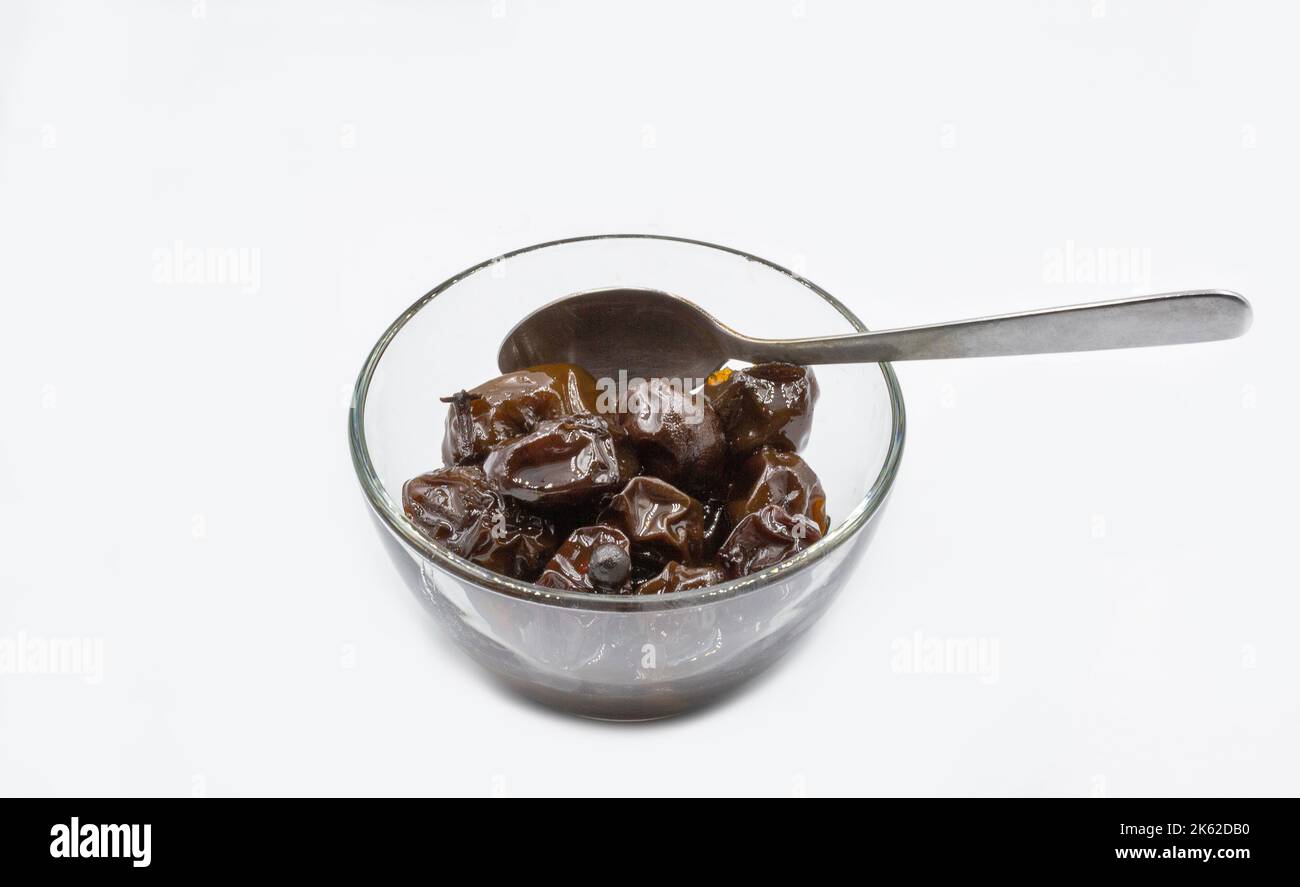 Prunes marinées dans un bol en verre, gros plan sur du blanc Banque D'Images