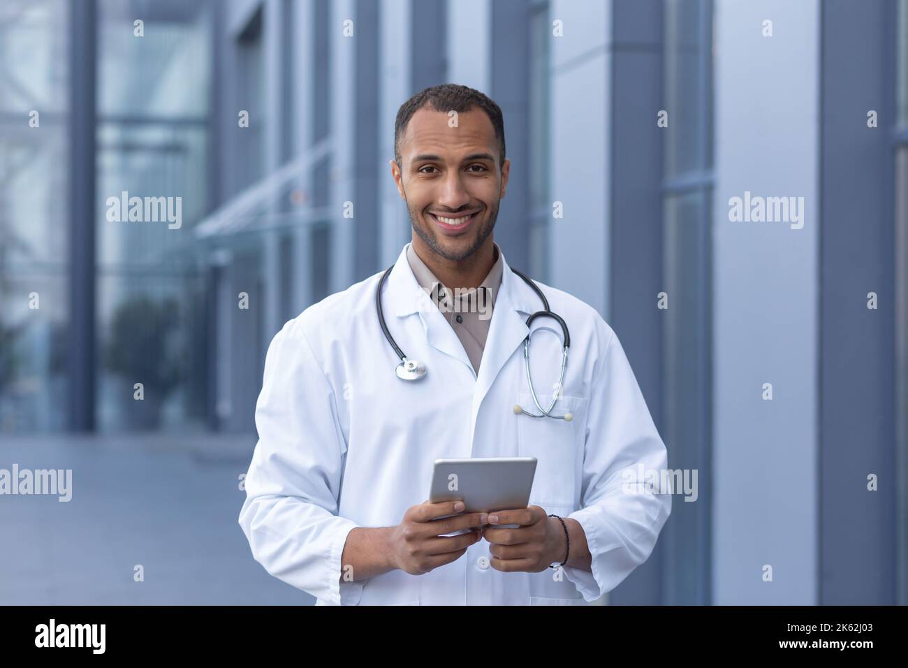 Portrait d'un médecin hispanique heureux et souriant, homme souriant et regardant l'appareil photo, médecin utilisant une tablette informatique pour la consultation en ligne, en dehors de la clinique moderne. Banque D'Images
