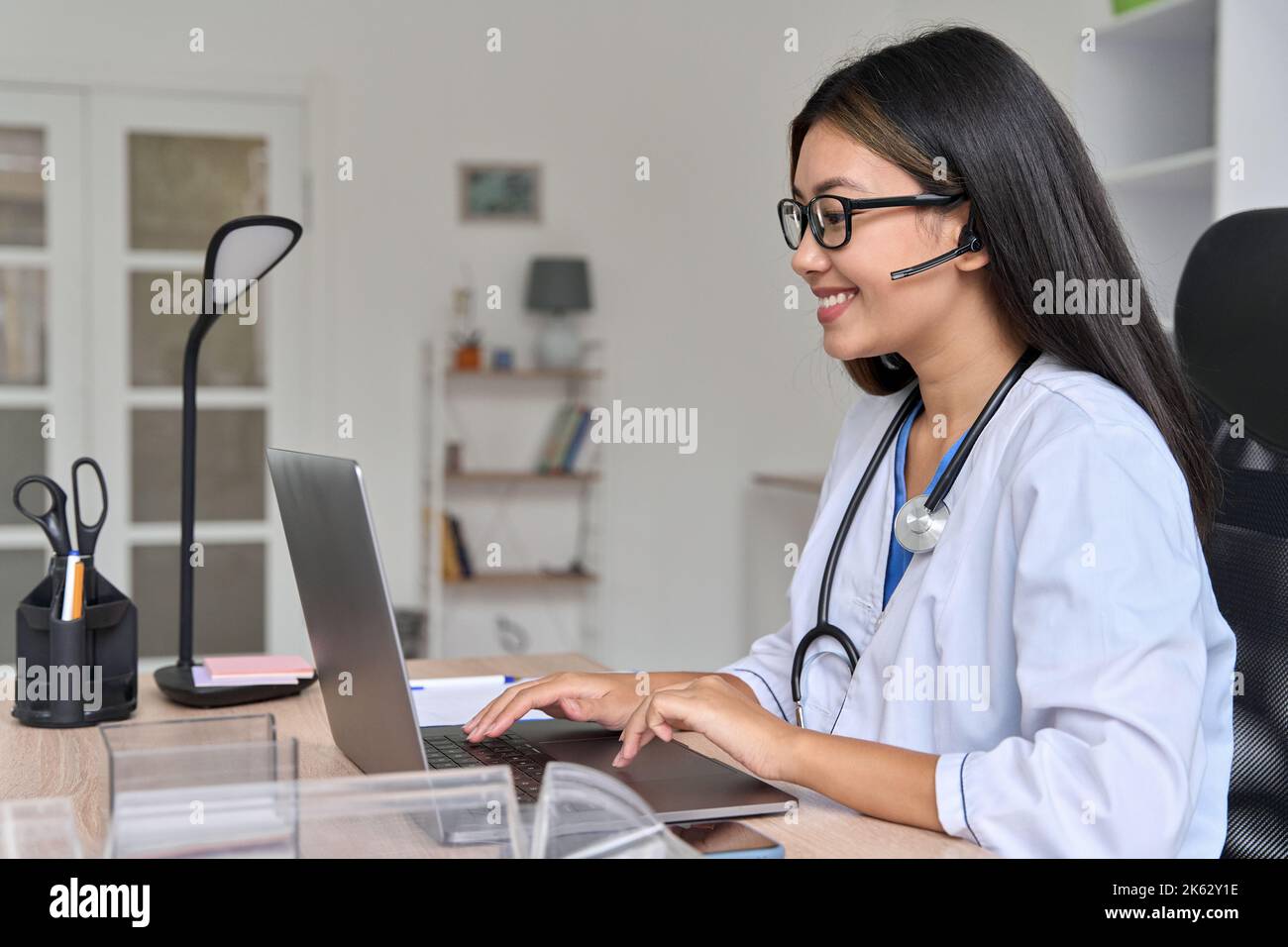 Vue latérale sur un jeune médecin asiatique communiquant en ligne avec un patient sur un ordinateur portable Banque D'Images
