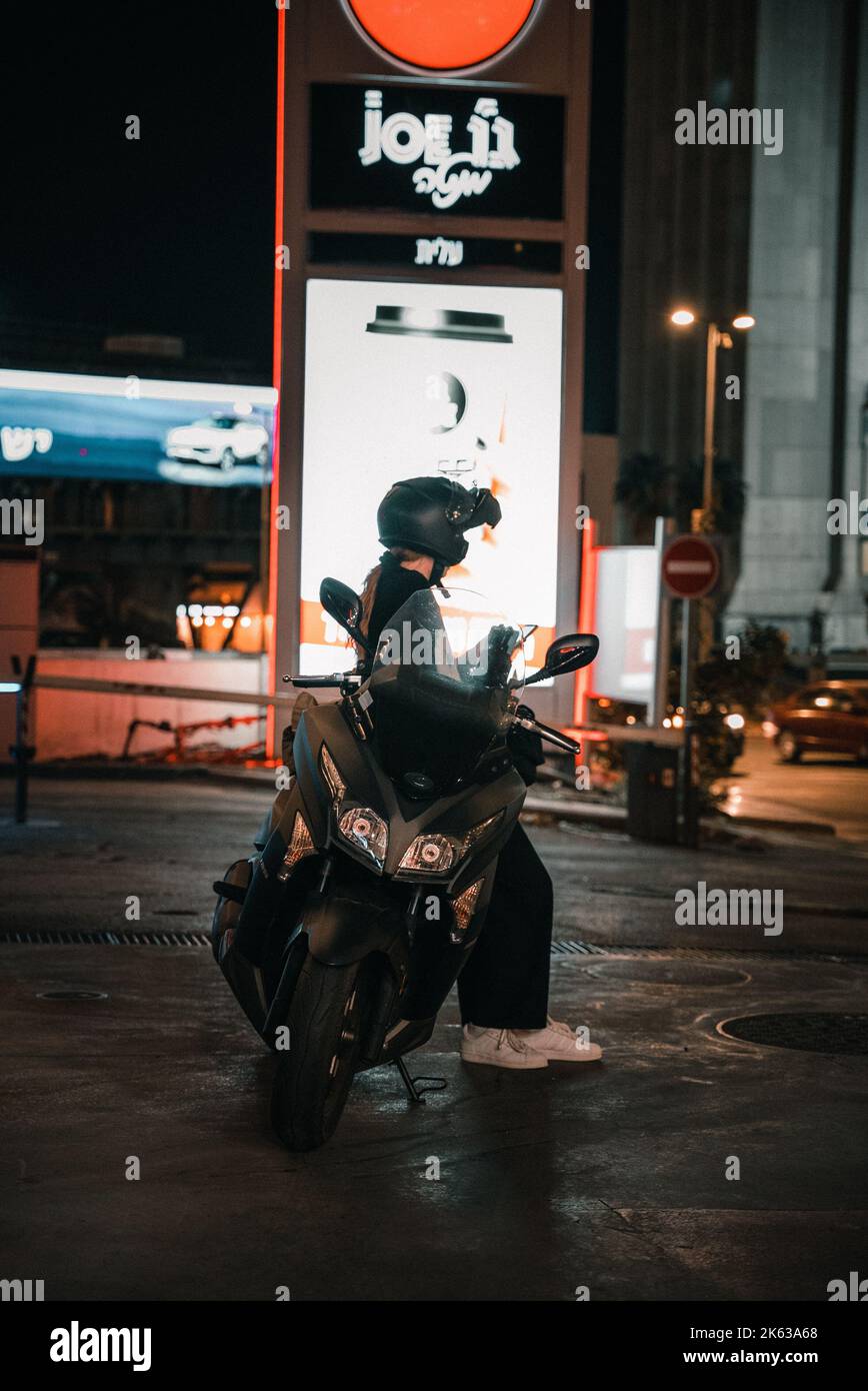Une jeune fille s'est penchée sur sa moto à la station-service la nuit. Banque D'Images