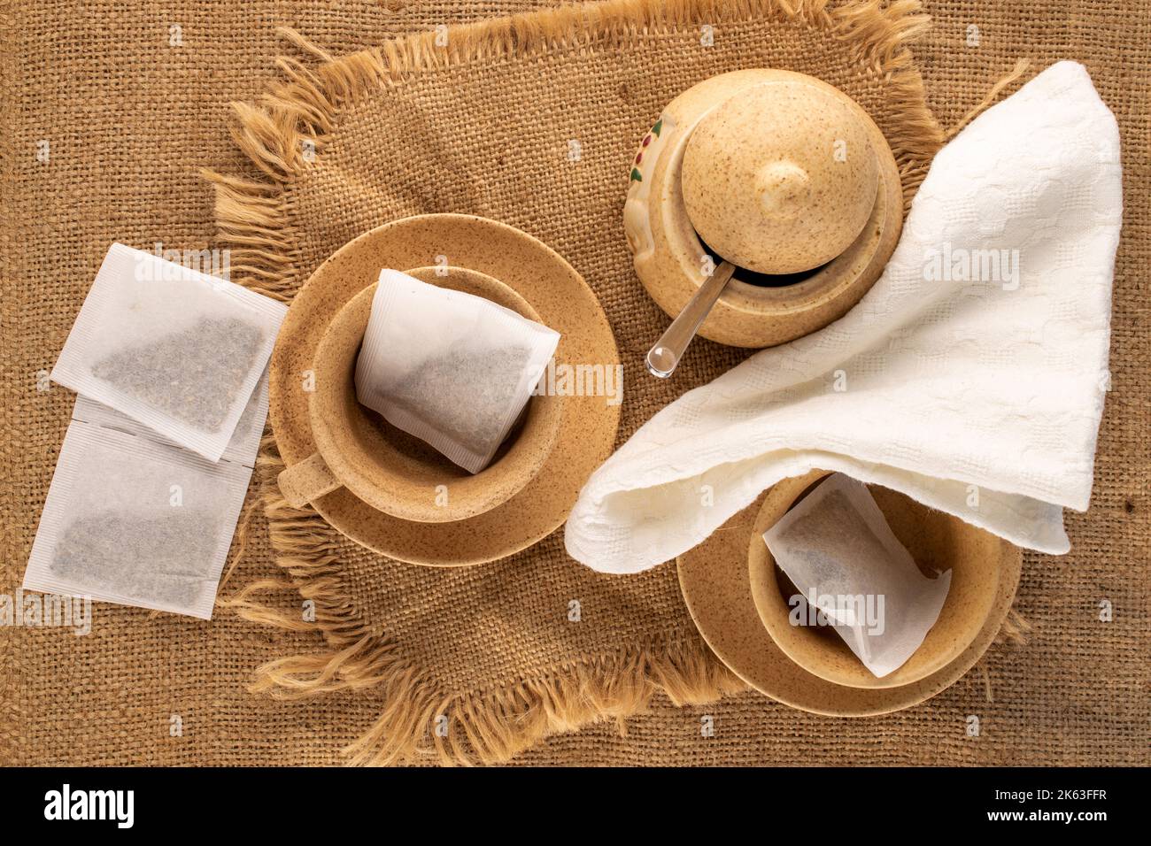 Plusieurs sachets de thé aromatiques avec vaisselle en céramique sur toile de jute, macro, vue de dessus. Banque D'Images