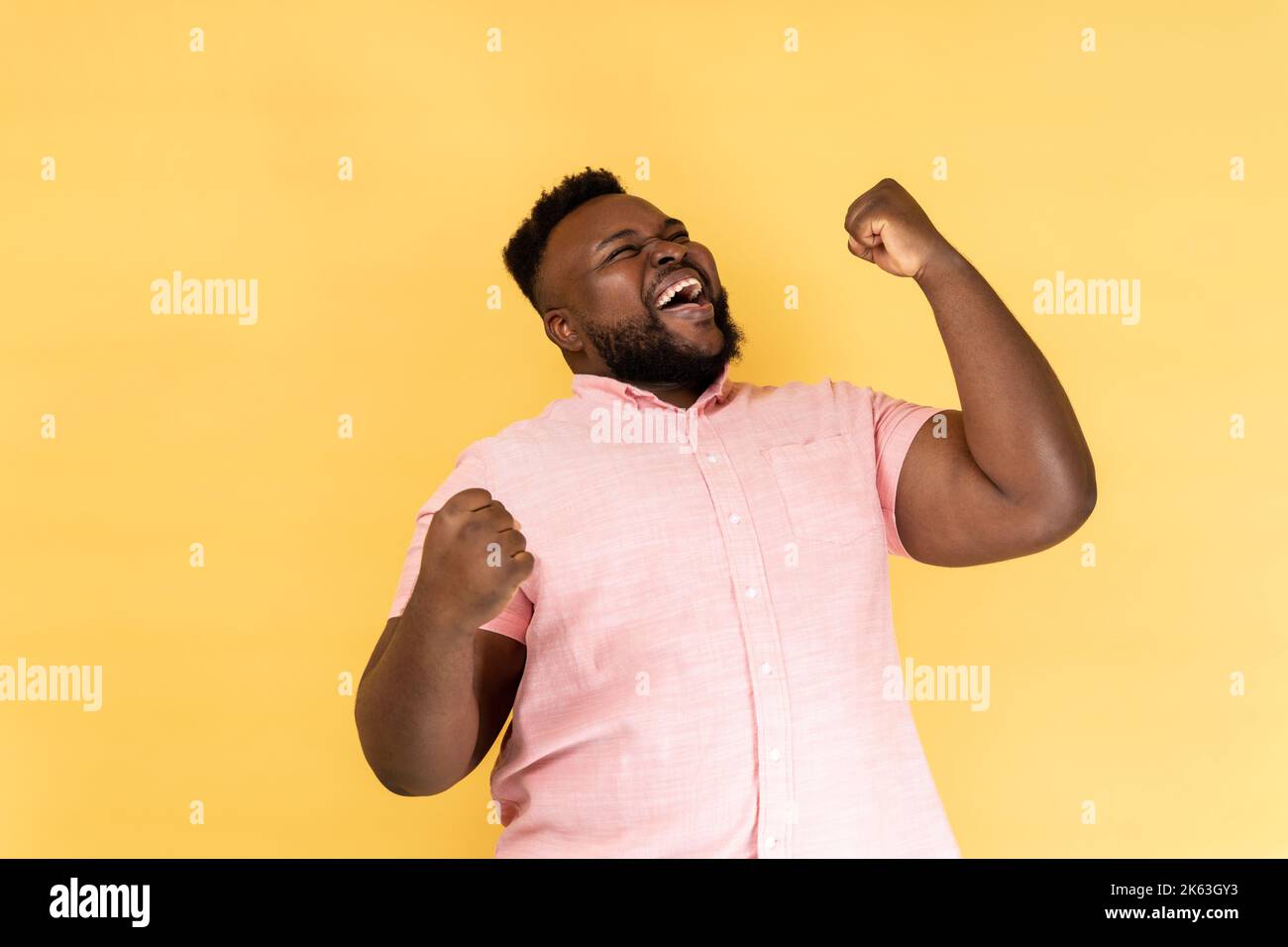 Portrait d'un homme extrêmement heureux portant une chemise rose célébrant son succès, debout avec des poings serrés, criant heureusement. Studio d'intérieur isolé sur fond jaune. Banque D'Images Portrait d'un homme extrêmement heureux portant une chemise rose célébrant son succès, debout avec des poings serrés, criant heureusement. Studio d'intérieur isolé sur fond jaune. Banque D'Images